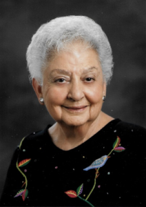 Smiley woman with short grey hair in black sweater with bird and nature embroidered motif.